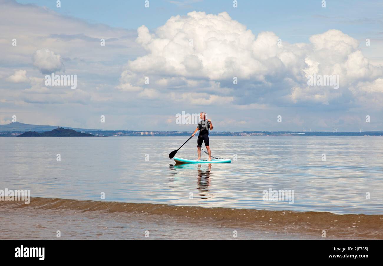 Portobello,Edinburgh, Scotland, UK. 30th June 2022. Cumulus clouds above and a mirror like surface on the calm Firth of Forth for this Stand Up Paddleboarder exercising early afternoon, with a temperature of 18 degrees centigrade. Credit: Archwhite/alamy live news. Stock Photo