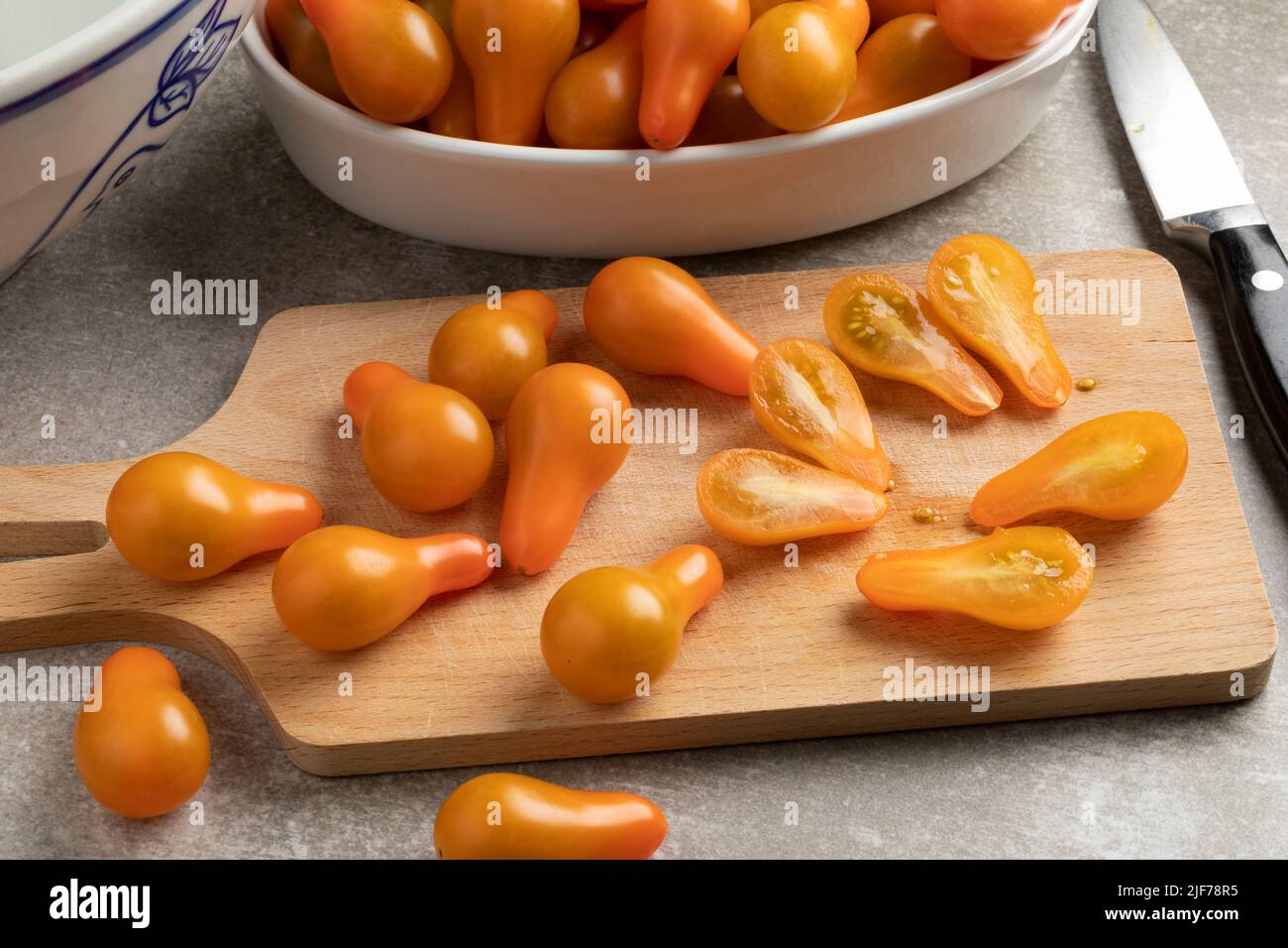 Cutting board with yellow whole and halved pear tomatoes close up in the kitchen Stock Photo