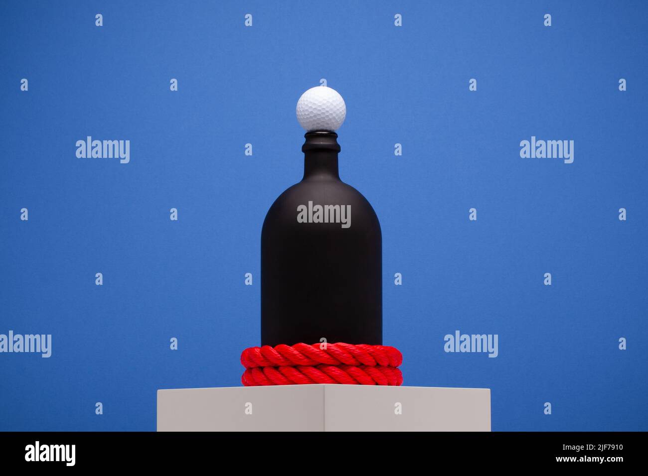Golf ball on mouth of black bottle on the blue background. Creative photography. Stock Photo