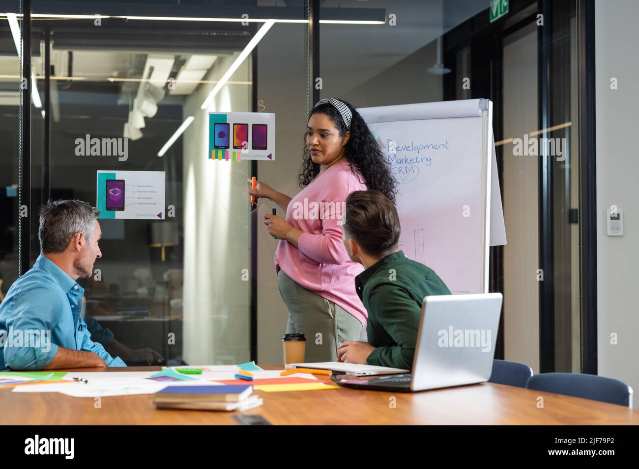 Young biracial businesswoman explaining strategy to colleagues over flipchart in meeting at office Stock Photo