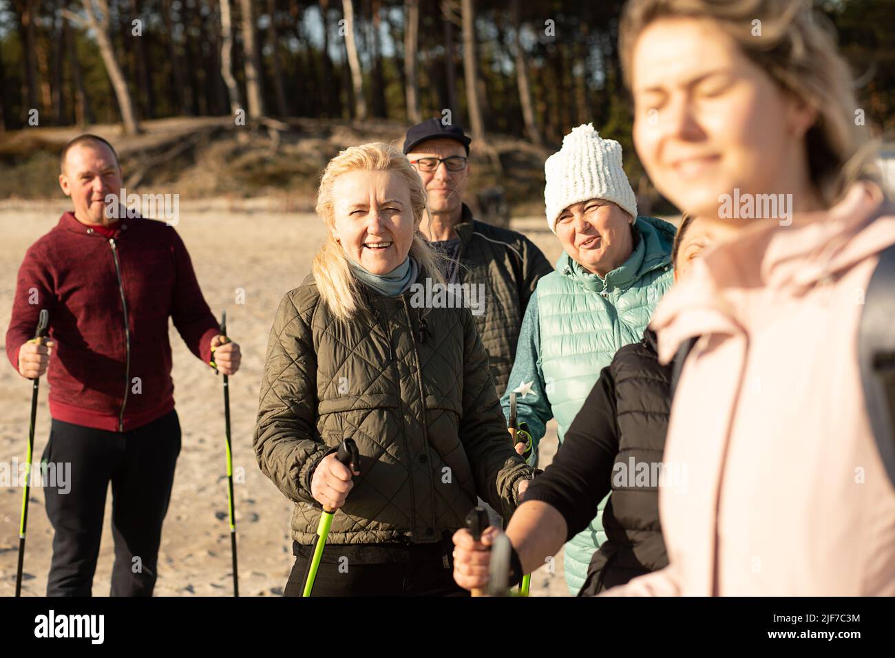 Joying woman blinking in the sunlight and people group, Nordic walking with trekking sticks, traveling forward outdoors Stock Photo