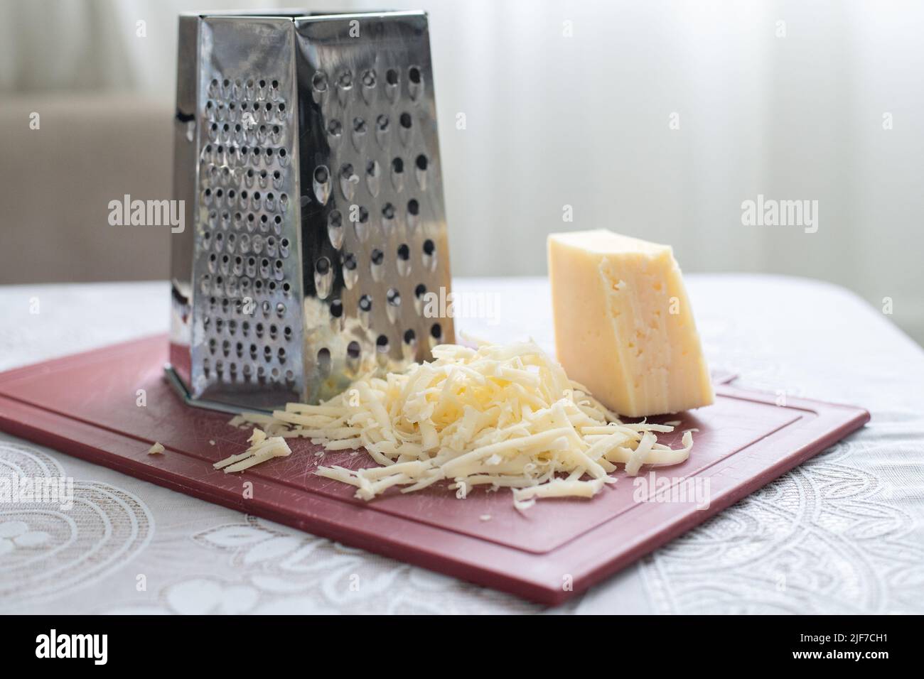A pile of grated cheese on a plastic board next to a grater Stock Photo