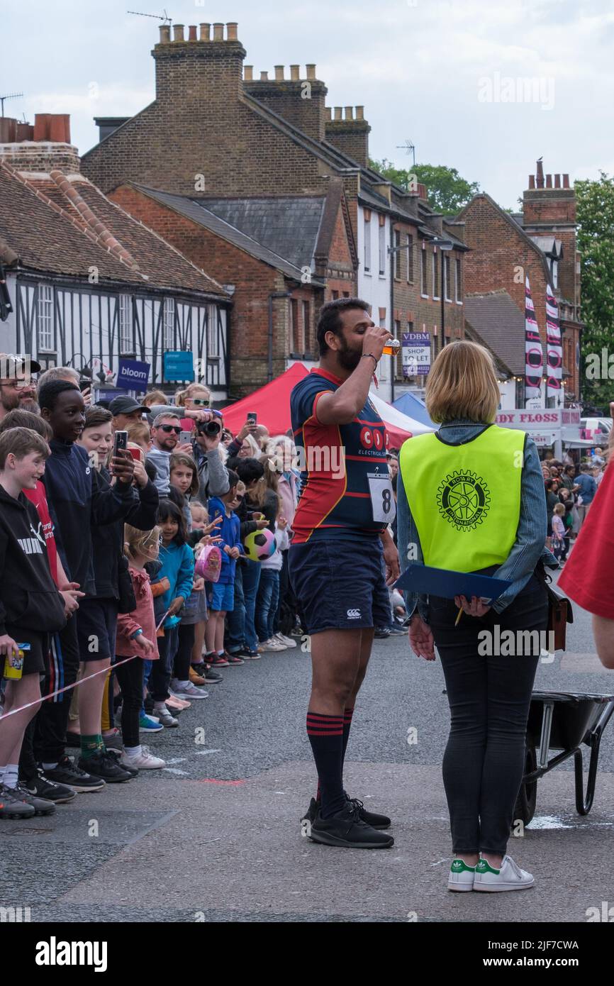 Race contestant stops to drink mandatory beer along the route of the wheelbarrow race, St George’s Day Celebration, Pinner, Harrow, NW London Stock Photo