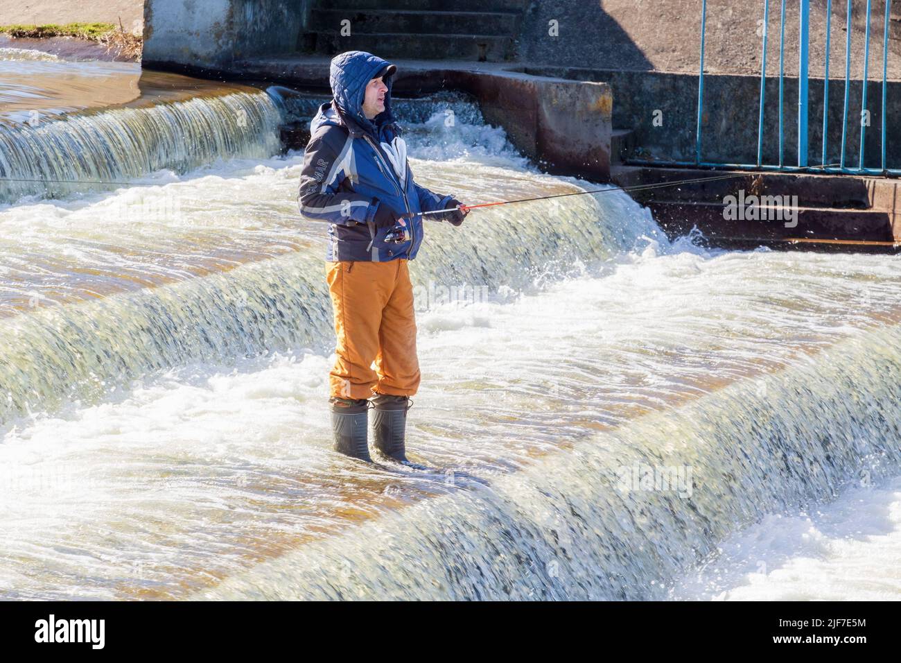 Minsk, Belarus - March 27, 2017: Man catches fish on a waterfall standing on a waterfall roll Stock Photo