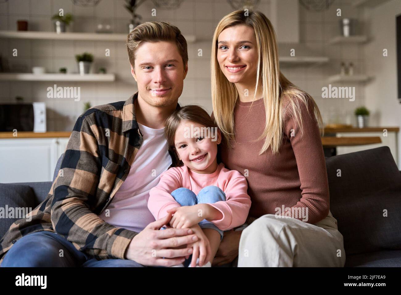 Happy family couple and child daughter bonding sitting on couch at home. Stock Photo