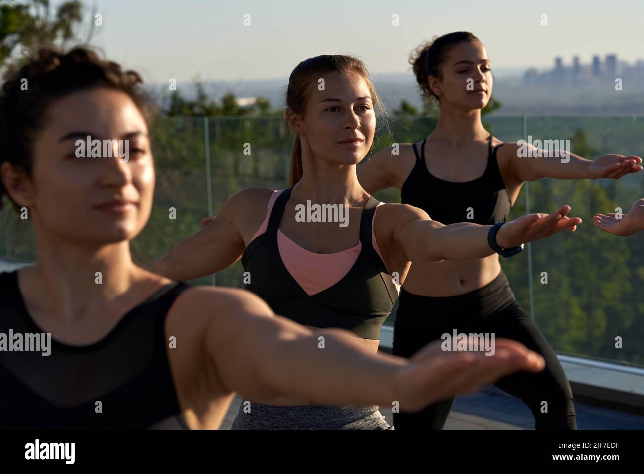 Fit healthy sporty women stand in yoga warrior pose at group class outdoor. Stock Photo