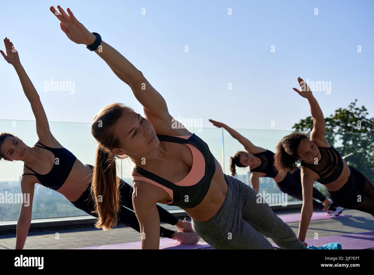Active fit sporty women stand in yoga side plank at outdoor group class. Stock Photo