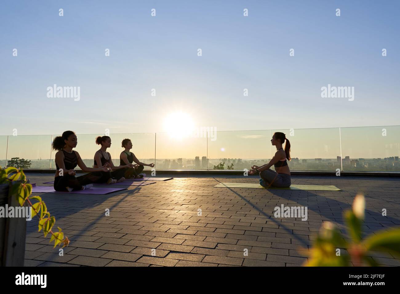 Multiethnic young women meditate with yoga teacher during group class outdoor. Stock Photo