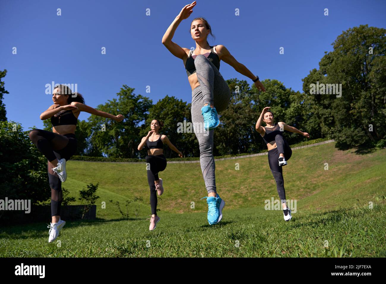 Active fit sporty women with fitness trainer jumping at outdoor group class. Stock Photo