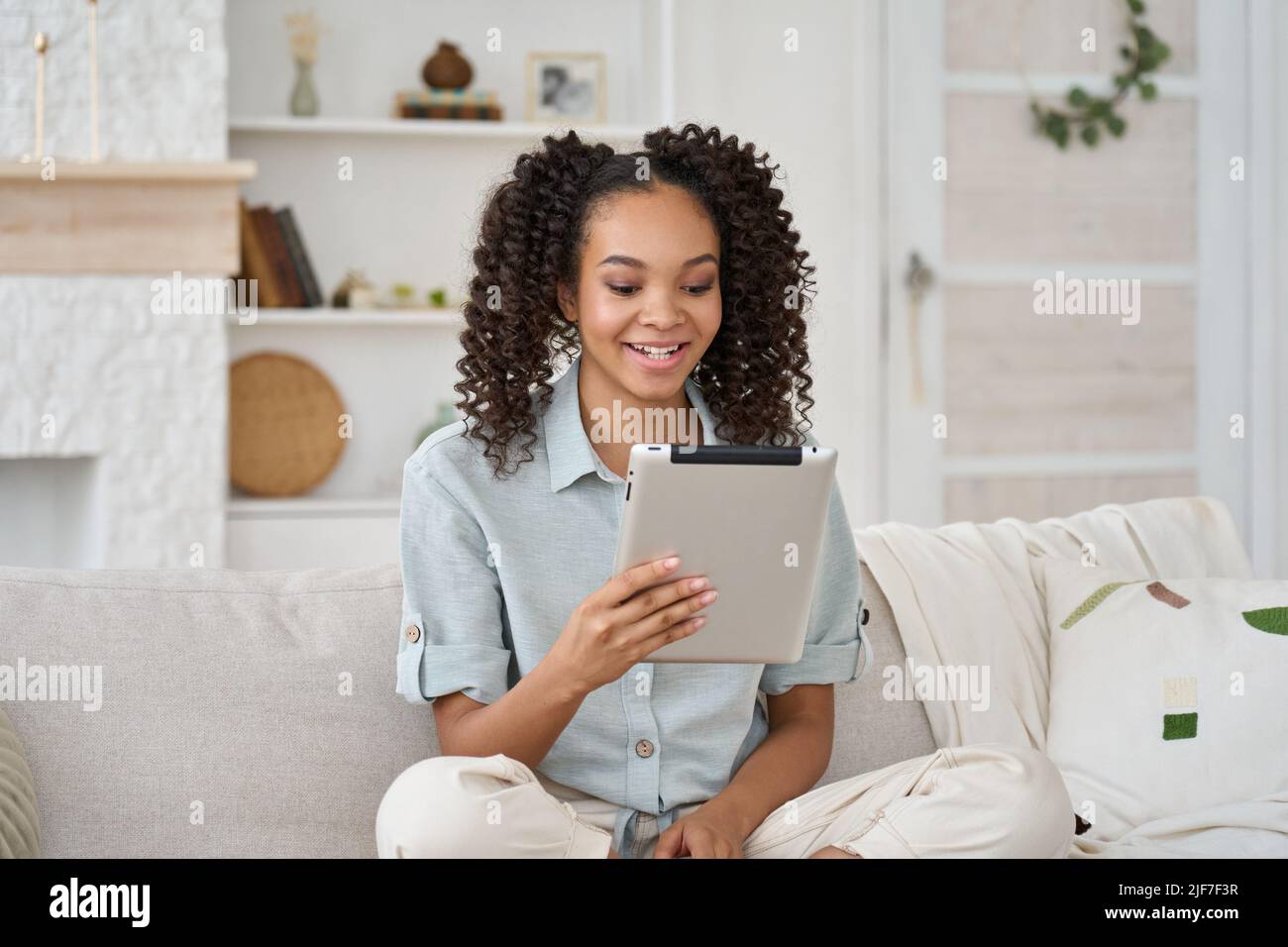 Joyful happy African American pretty teenage girl using digital tablet at home. Stock Photo