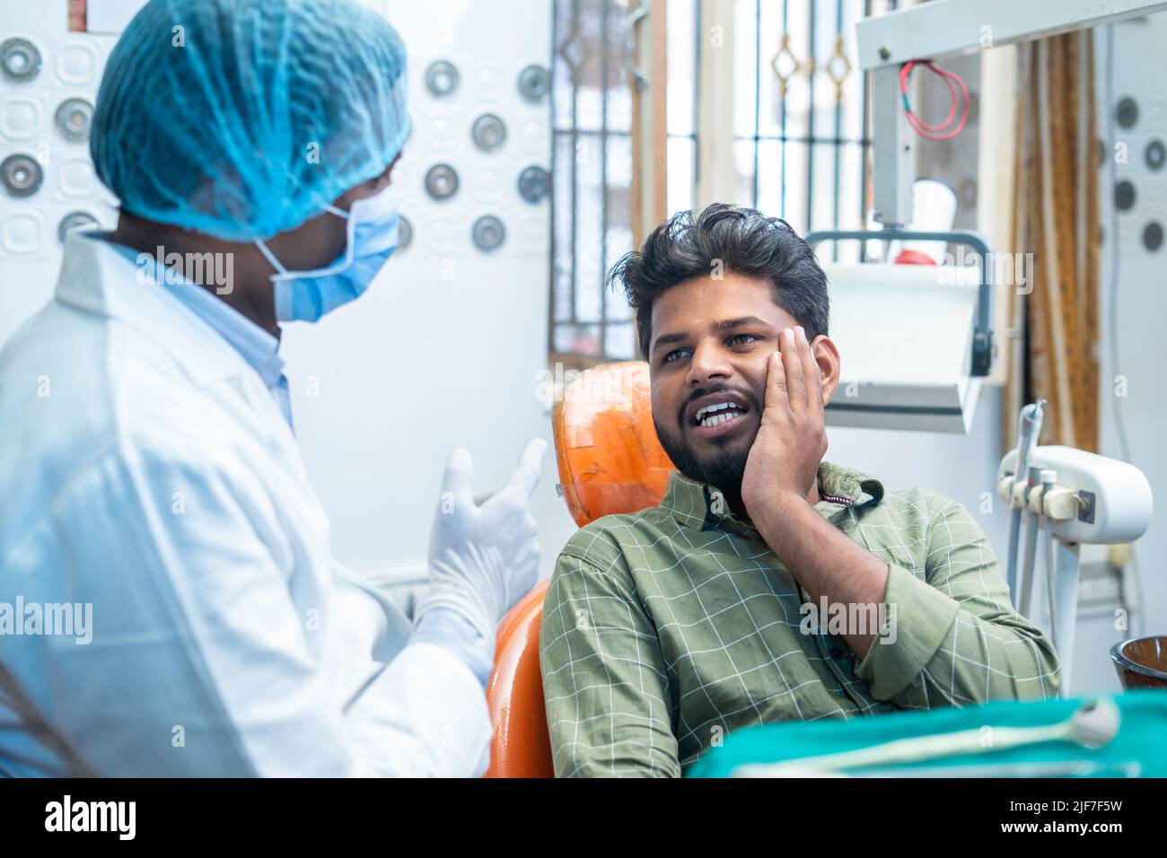 suffering young man explaining about toothache or cavity to dentist at hospital - concept of conversation, oral treatment and hygienist Stock Photo