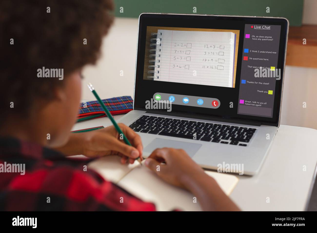 African american girl with afro hair writing maths in book from laptop screen during online class Stock Photo