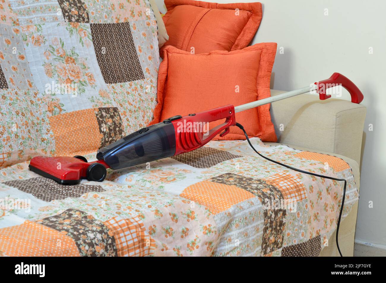 Red vacuum cleaner on couch with colored fabric cover, with pillows of different colors, panoramic photo Stock Photo