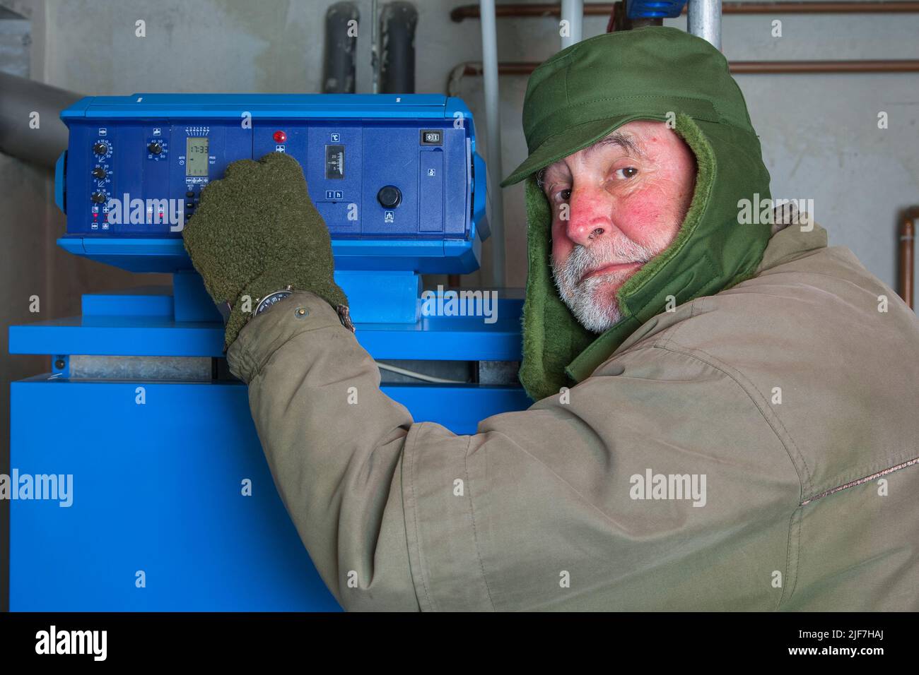 Old man with thick winter clothes and a red face turns down his gas heater. Energy prices have exploded and many people cannot afford to keep their ho Stock Photo