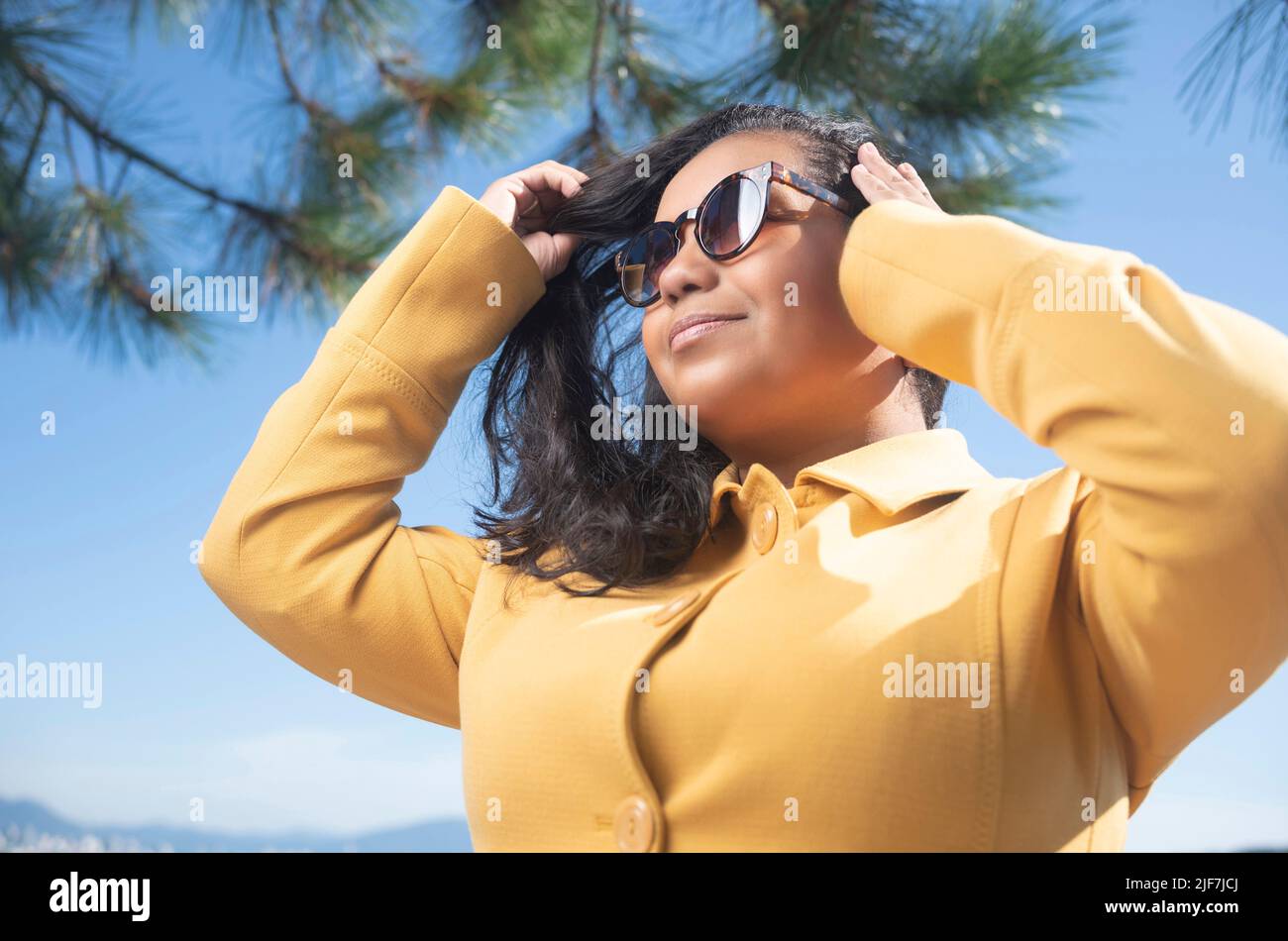 Mid age afro woman wearing sun glasses and yellow coat Stock Photo