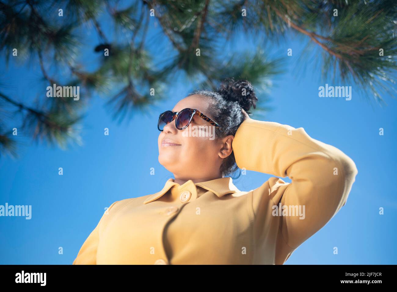 Afro woman wearing a yellow coat and sunglasses outdoors Stock Photo