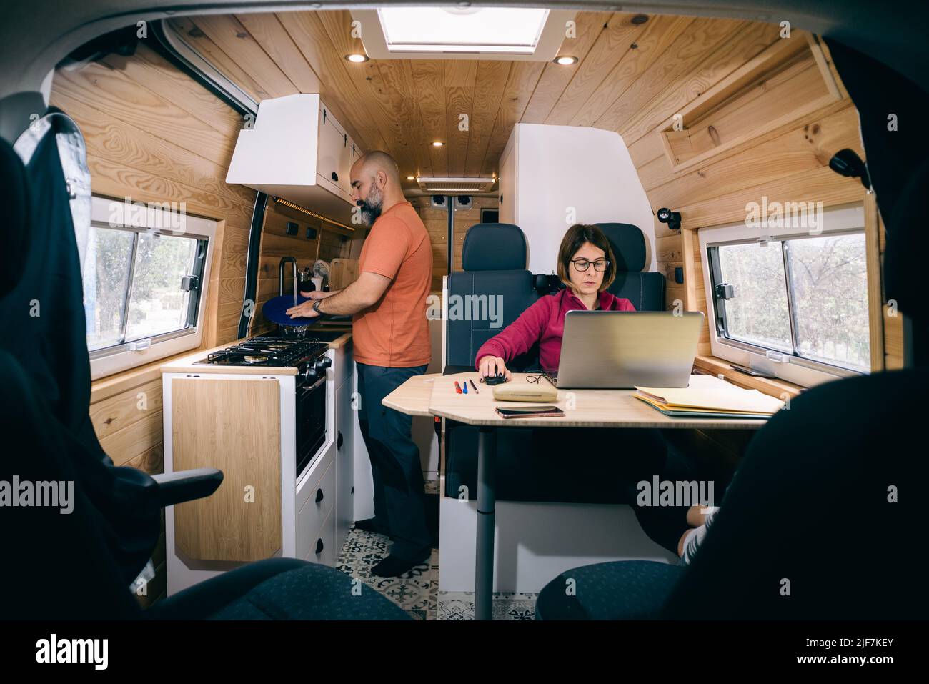 Couple living in a camper van. Woman teleworking. Man washing dishes. Stock Photo