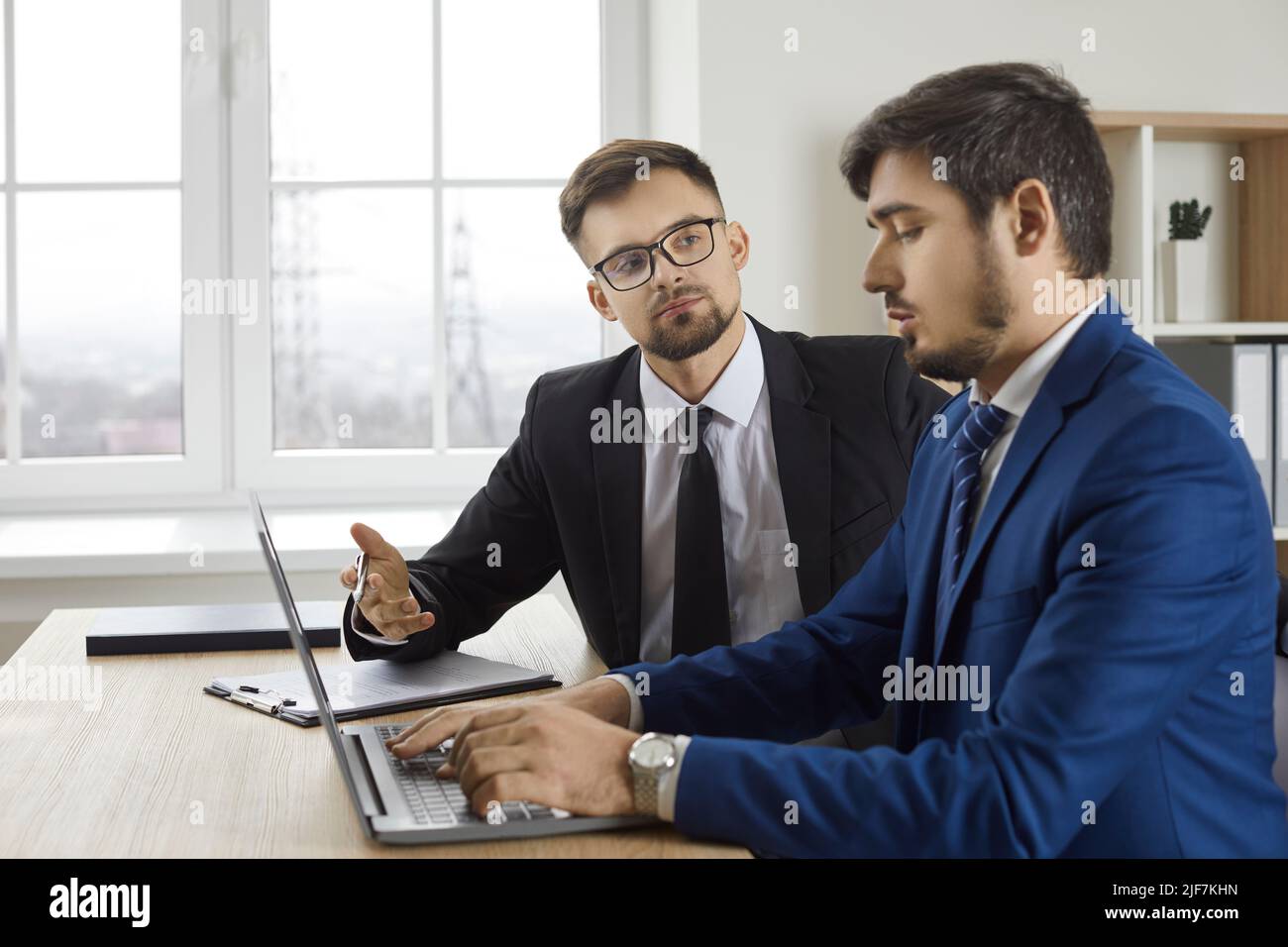 Two male business colleagues discuss new project together while working on it together in office. Stock Photo