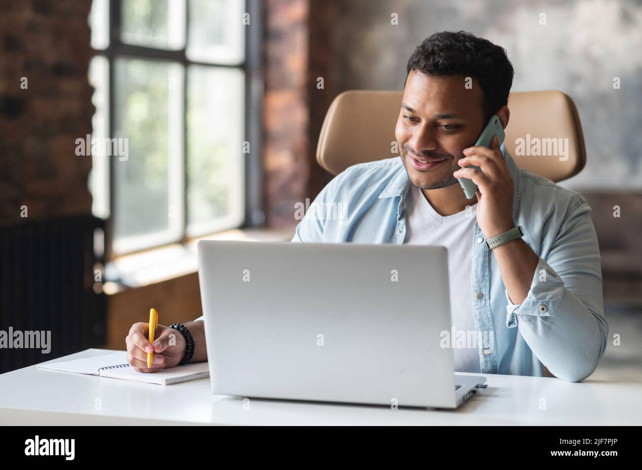 Smiling indian freelancer guy in casual wear sits at the desk in 