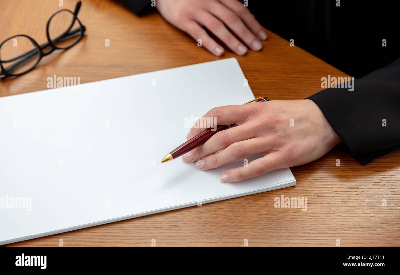 Woman holding a pen on a blank white paper, close up above view, wooden office table background. Female left hand signing on empty document, copy spac Stock Photo