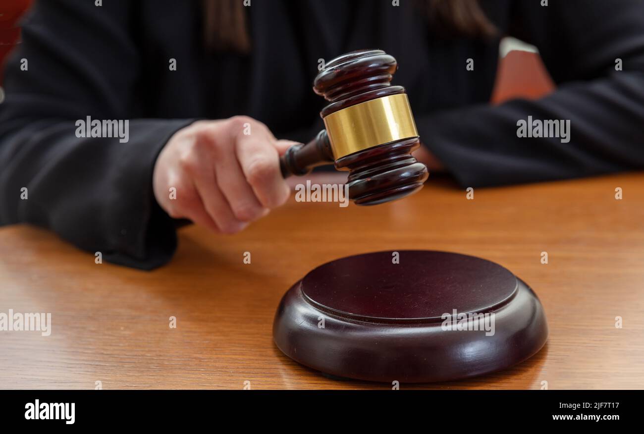 Judge female hand holding a prosecution gavel on wooden law court bench, close up front view. Justice and punishment concept Stock Photo