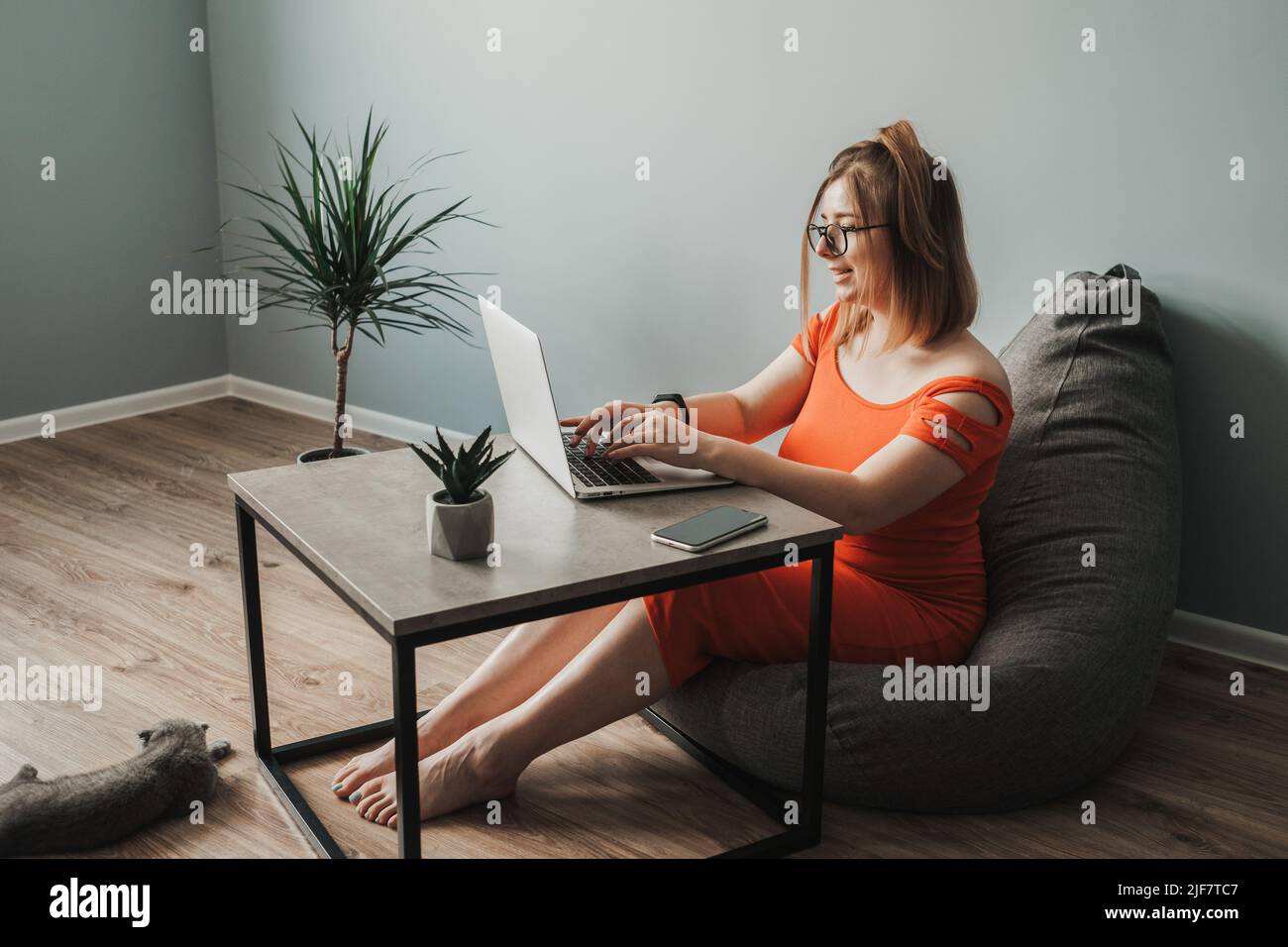 Caucasian Young Woman in the Red Dress Working by Laptop from Home, Female Freelancer at Work, Remote Job Stock Photo