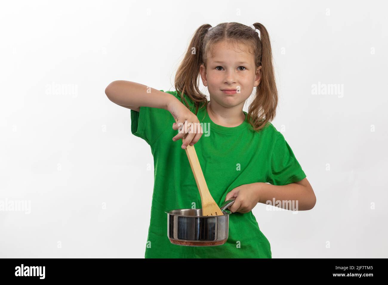 A young girl shows that she loves to cook with her wooden cooking spoon and stainless steel pot Stock Photo
