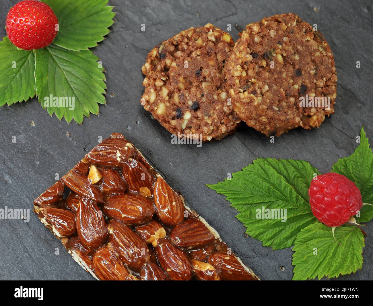 top view of almond bar and granola cookies with fruits, strawberry and raspberry with leaf, healthy high protein snack with nuts for sports nutrition Stock Photo
