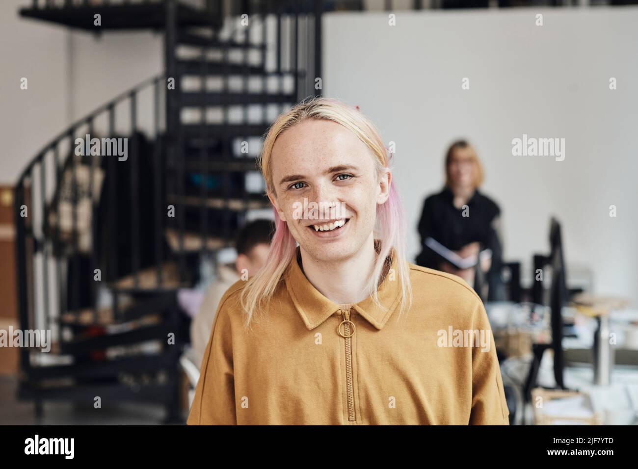 Portrait of smiling non-binary computer programmer with dyed long hair at tech start-up office Stock Photo
