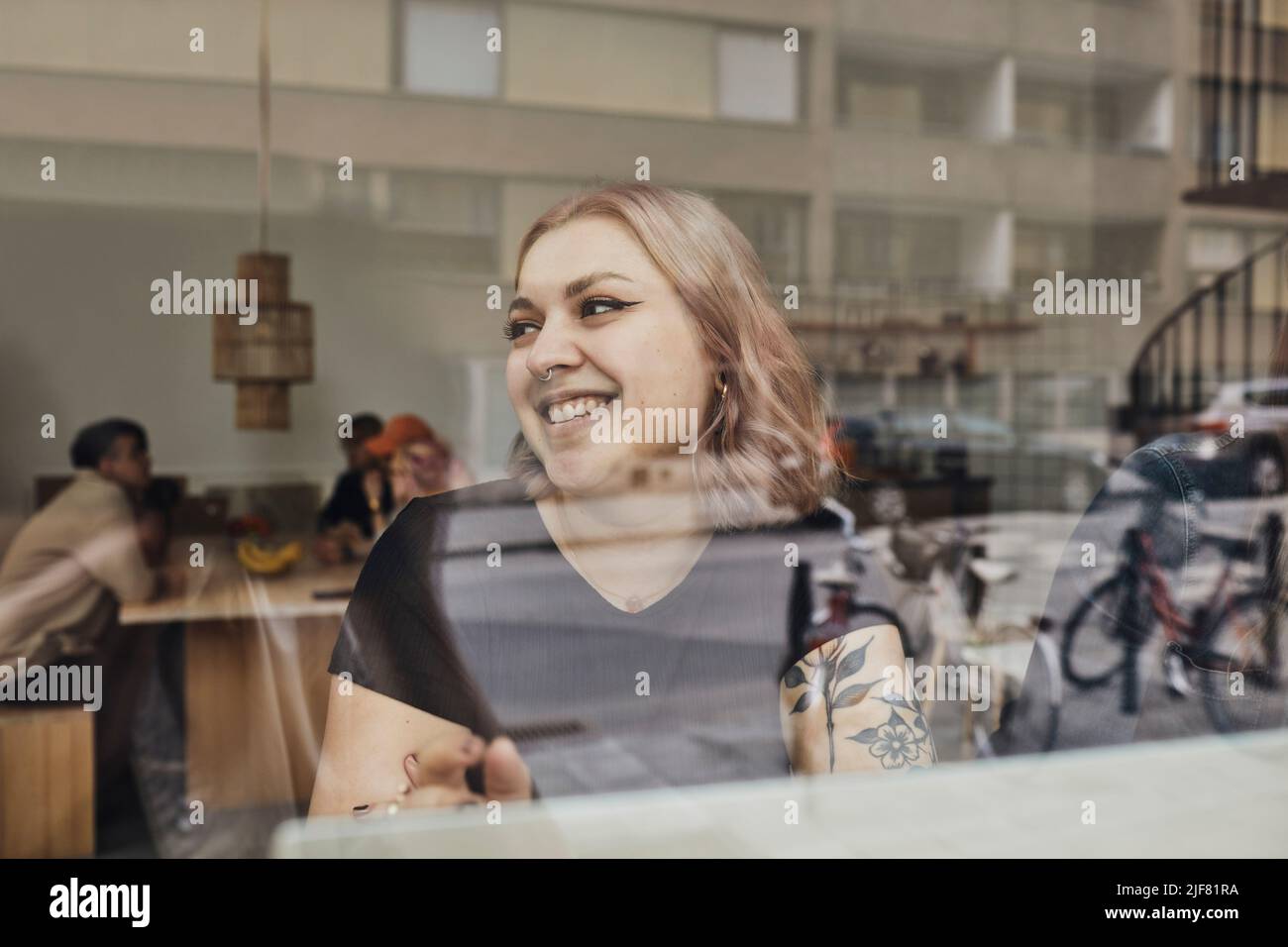 Happy female entrepreneur looking away while sitting in office seen through glass Stock Photo