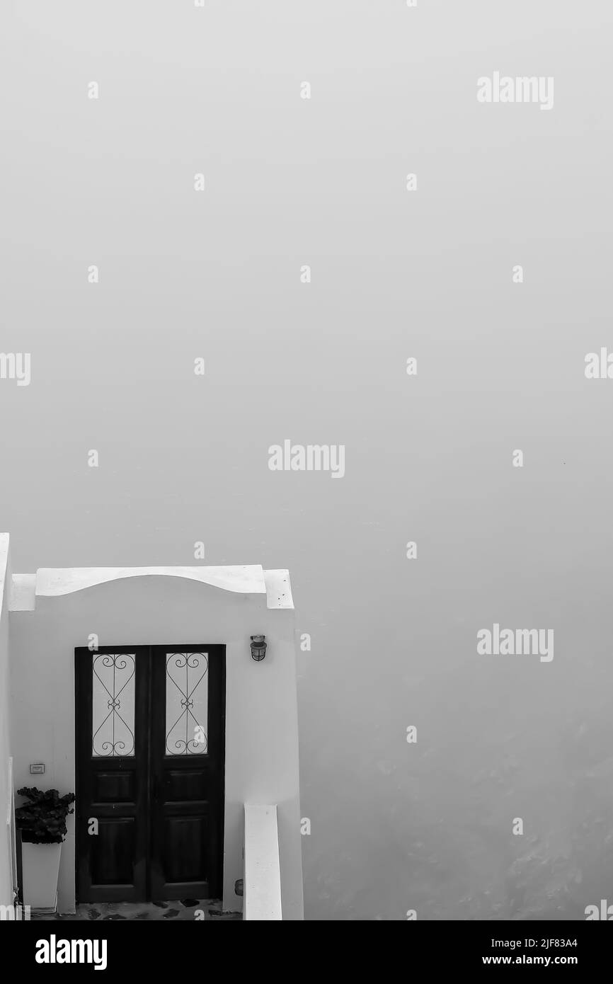 View of a decorative traditional door and view of the foggy Aegean Sea in the background in Santorini in black and white Stock Photo