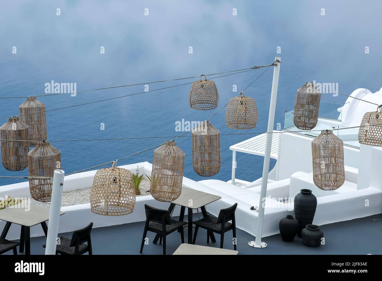 Santorini, Greece - May 13, 2021 :  View of a picturesque terrace decorated with tables, chairs  and lights overlooking the Aegean Sea Stock Photo