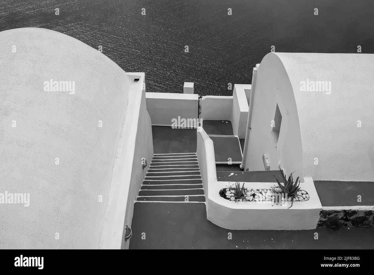 View of the steps of a typical whitewashed villa in Santorini and the Aegean Sea in the background in black and white Stock Photo