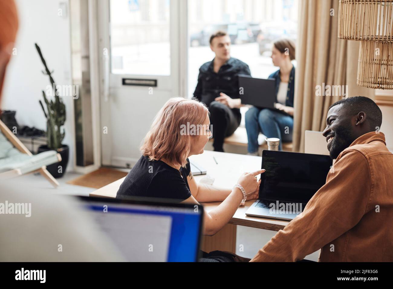 Businesswoman explaining male colleague over laptop while sitting in office Stock Photo