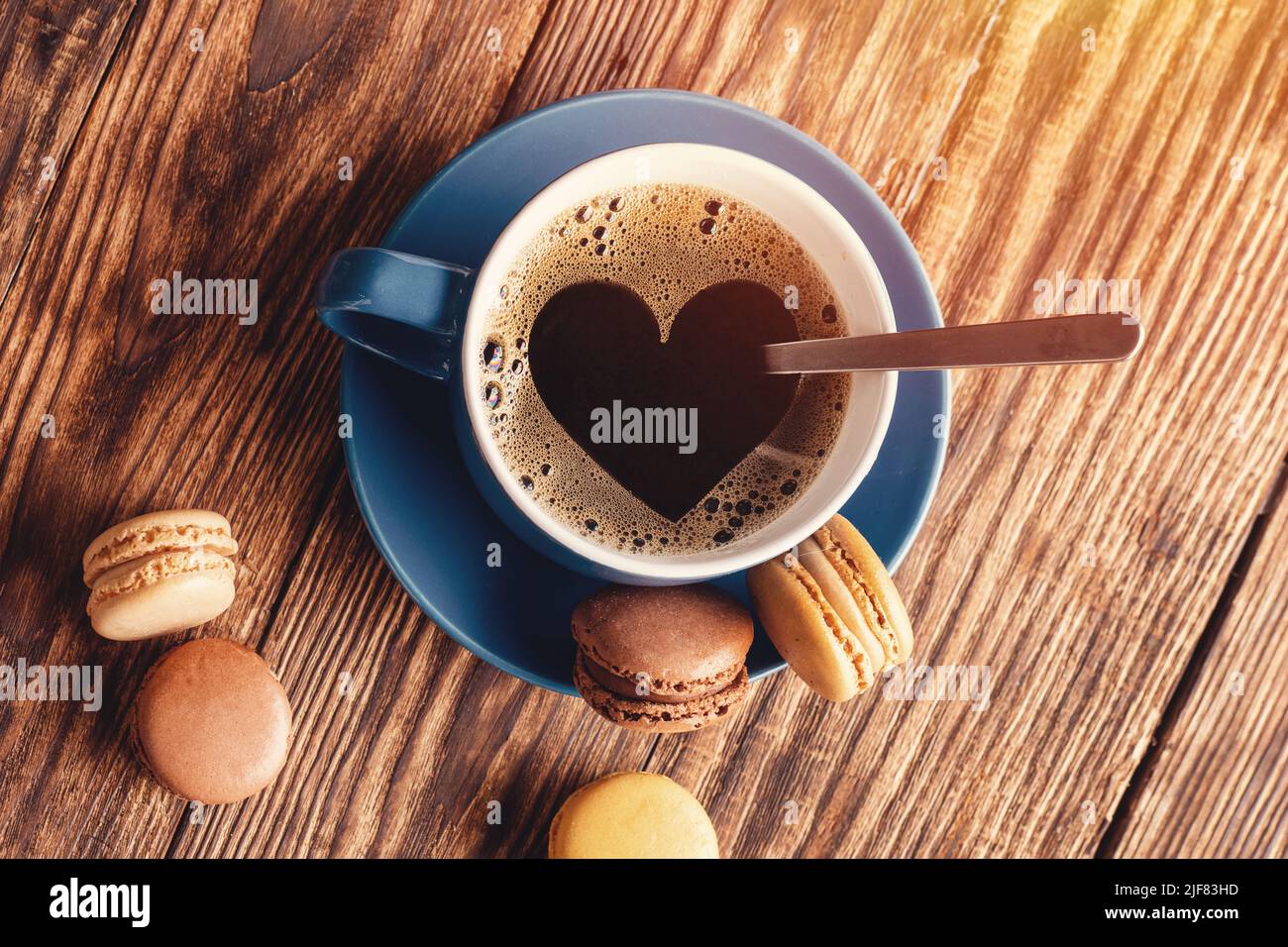 blue cup of coffee with heartshape  foam  and macaroons on the wooden background. Coffee is the good idea Stock Photo
