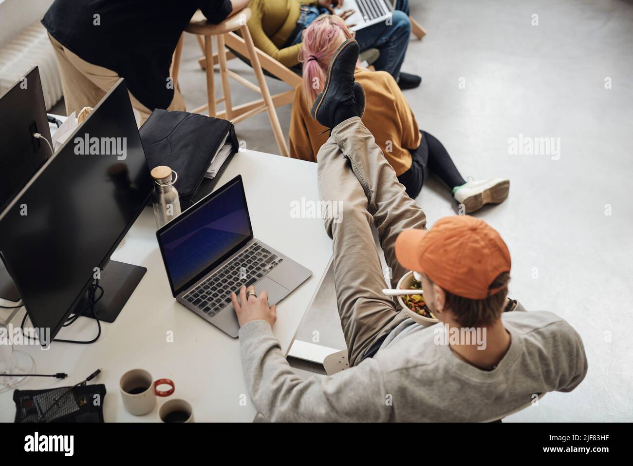 High angle view of male programmer with feet up on desk using laptop while eating lunch in office Stock Photo