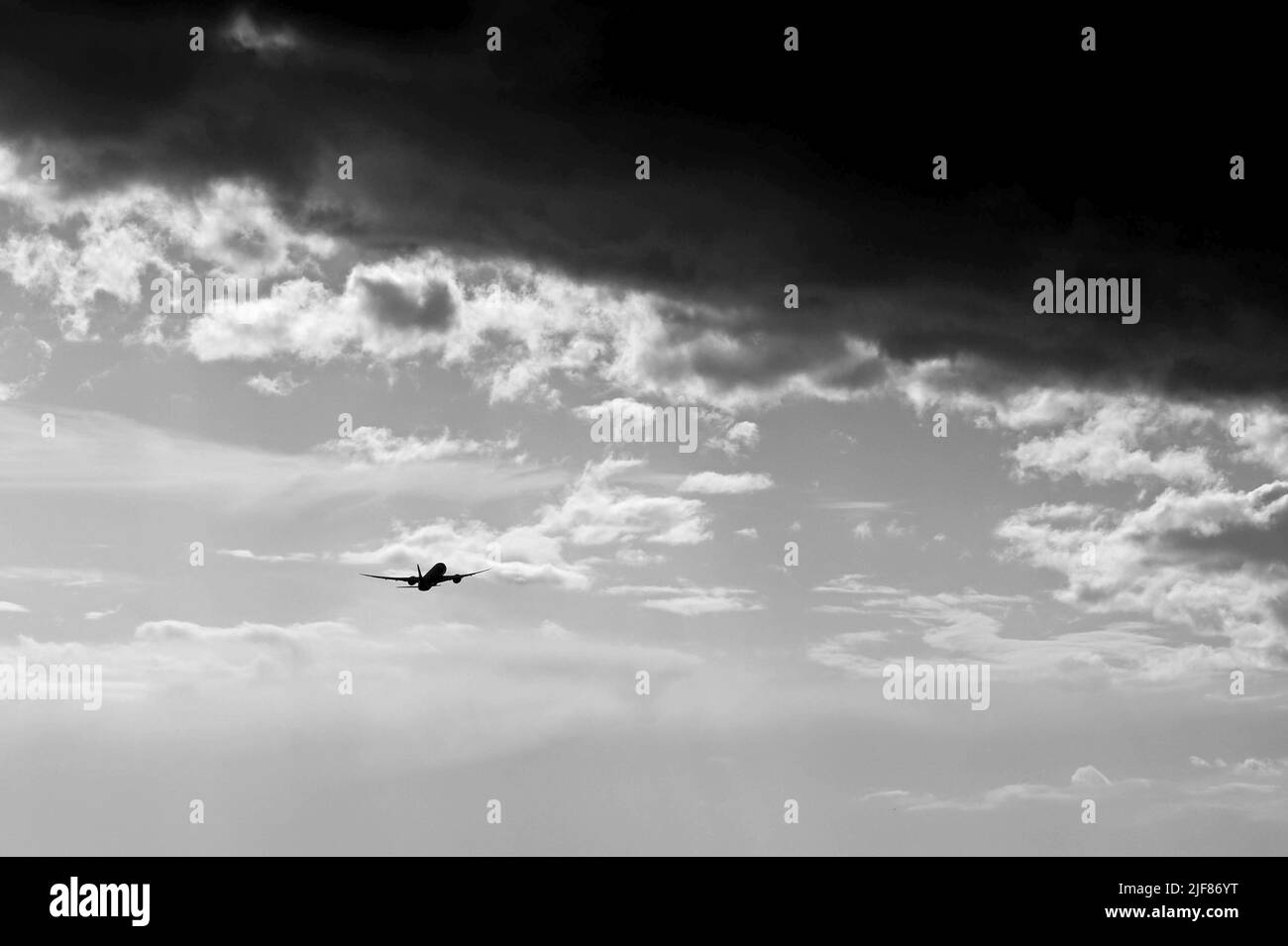 Silhouette of a passenger aircraft departing an airport with a large storm cloud overhead. Black and white image. No people. Copy space. Stock Photo