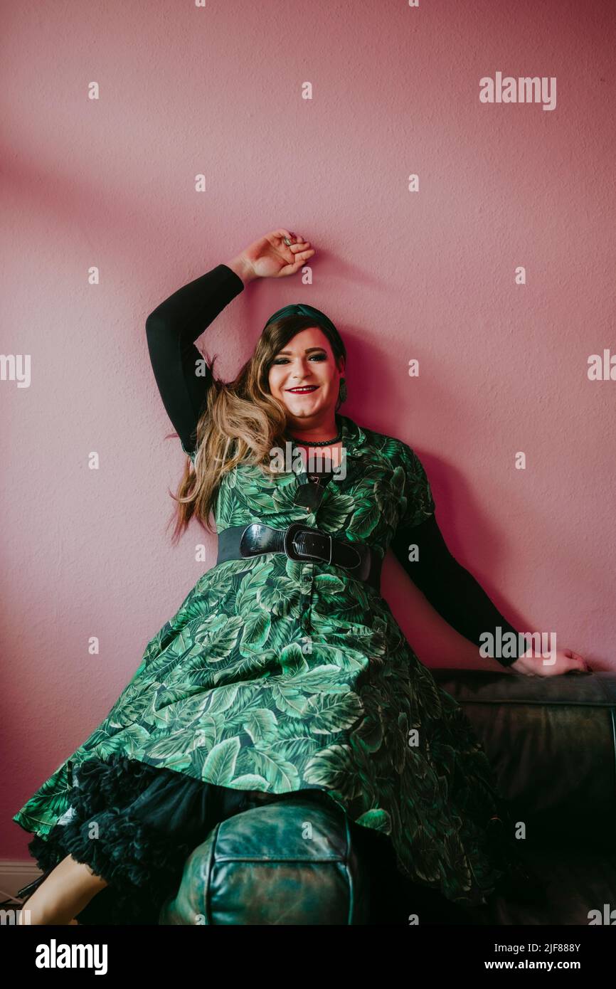 Portrait of smiling non-gender person sitting on sofa against pink wall at home Stock Photo