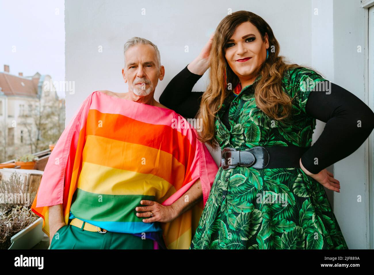 Portrait of mature gay man standing by non-binary friend on balcony ...