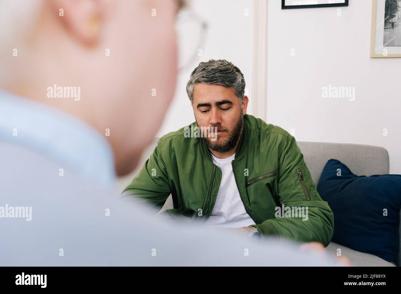 Depressed man taking advice from female psychotherapist in therapy office Stock Photo