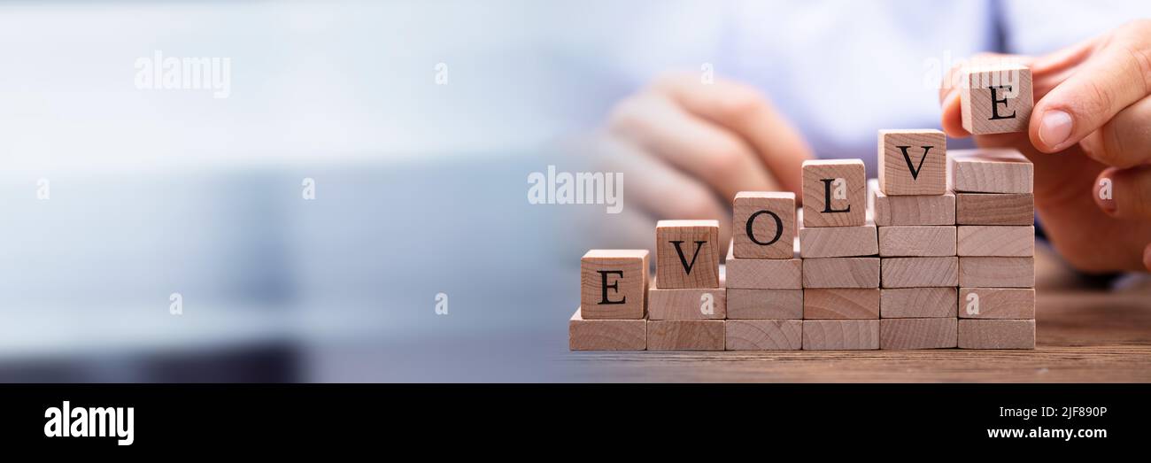 Close-up Of Person's Hand Placing Last Alphabet Of Word Evolve On Wooden Block Stock Photo