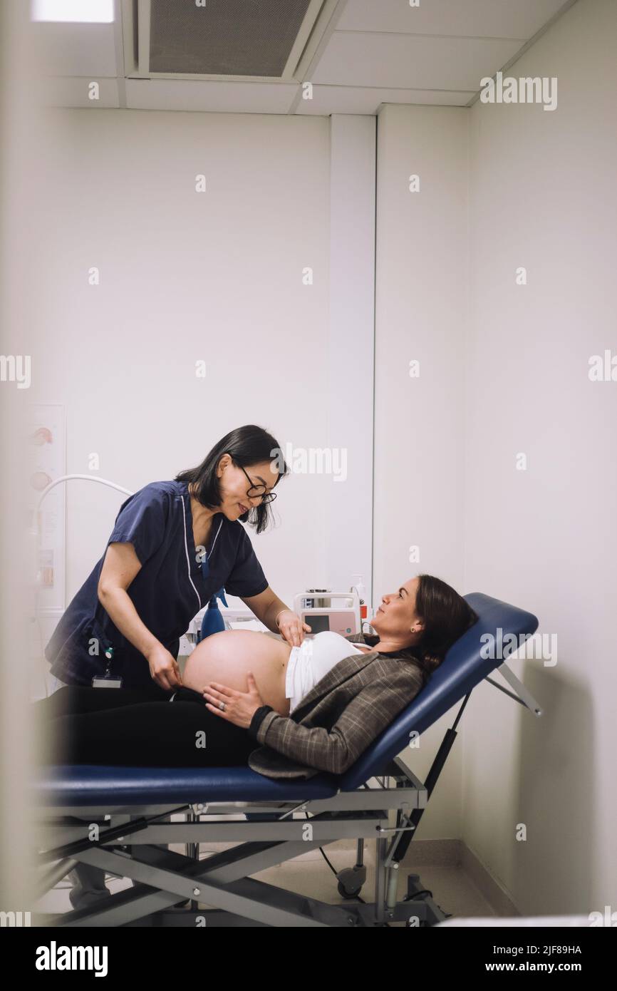 Female healthcare expert measuring abdomen of pregnant woman lying on gurney in medical clinic Stock Photo