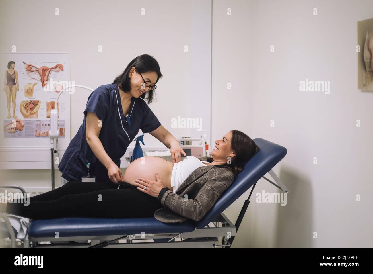 Smiling female doctor measuring abdomen of pregnant woman while examining in medical clinic Stock Photo
