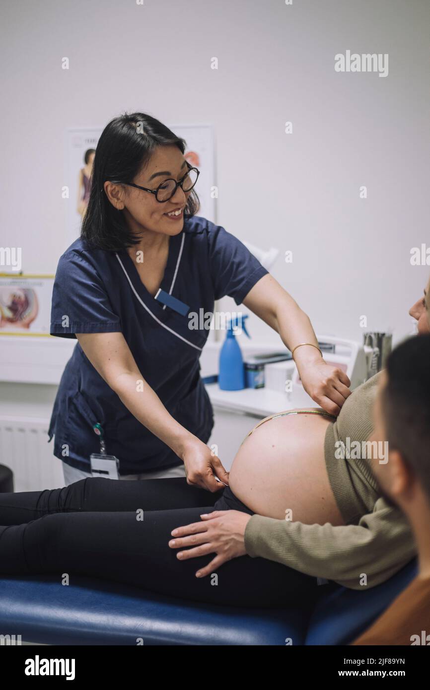Smiling female doctor measuring abdomen of pregnant woman in medical clinic Stock Photo