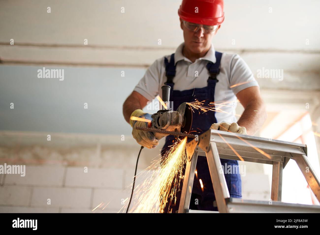 Professional construction worker hands in work gloves using angle grinder to cut metal rod at building site. Close up shot of contractor cutting iron Stock Photo