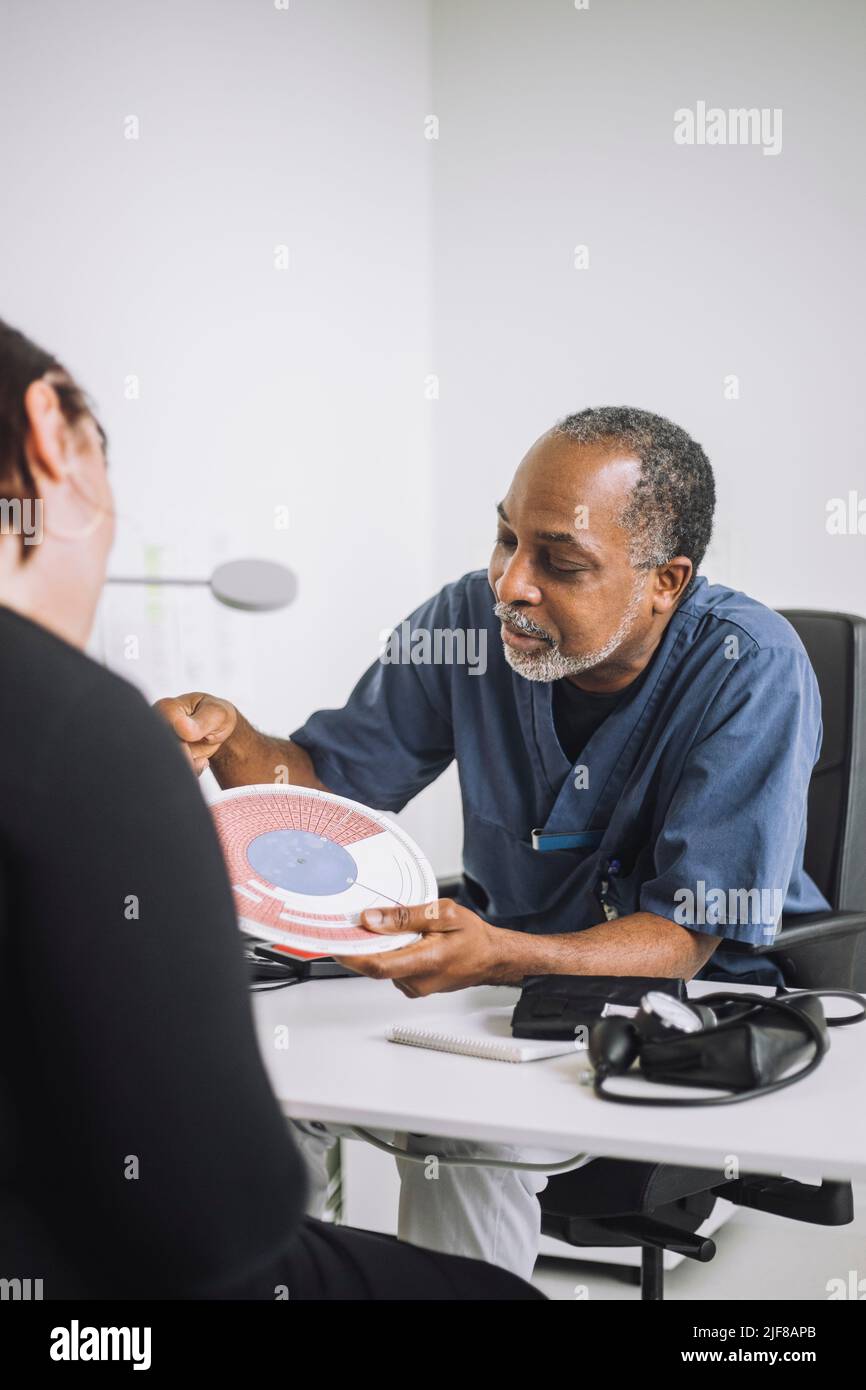 Mature male doctor discussing over in vitro fertilization chart with female patient sitting at desk in medical clinic Stock Photo