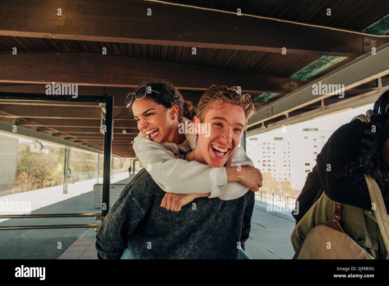 Happy young man piggybacking female friend at railroad station platform Stock Photo