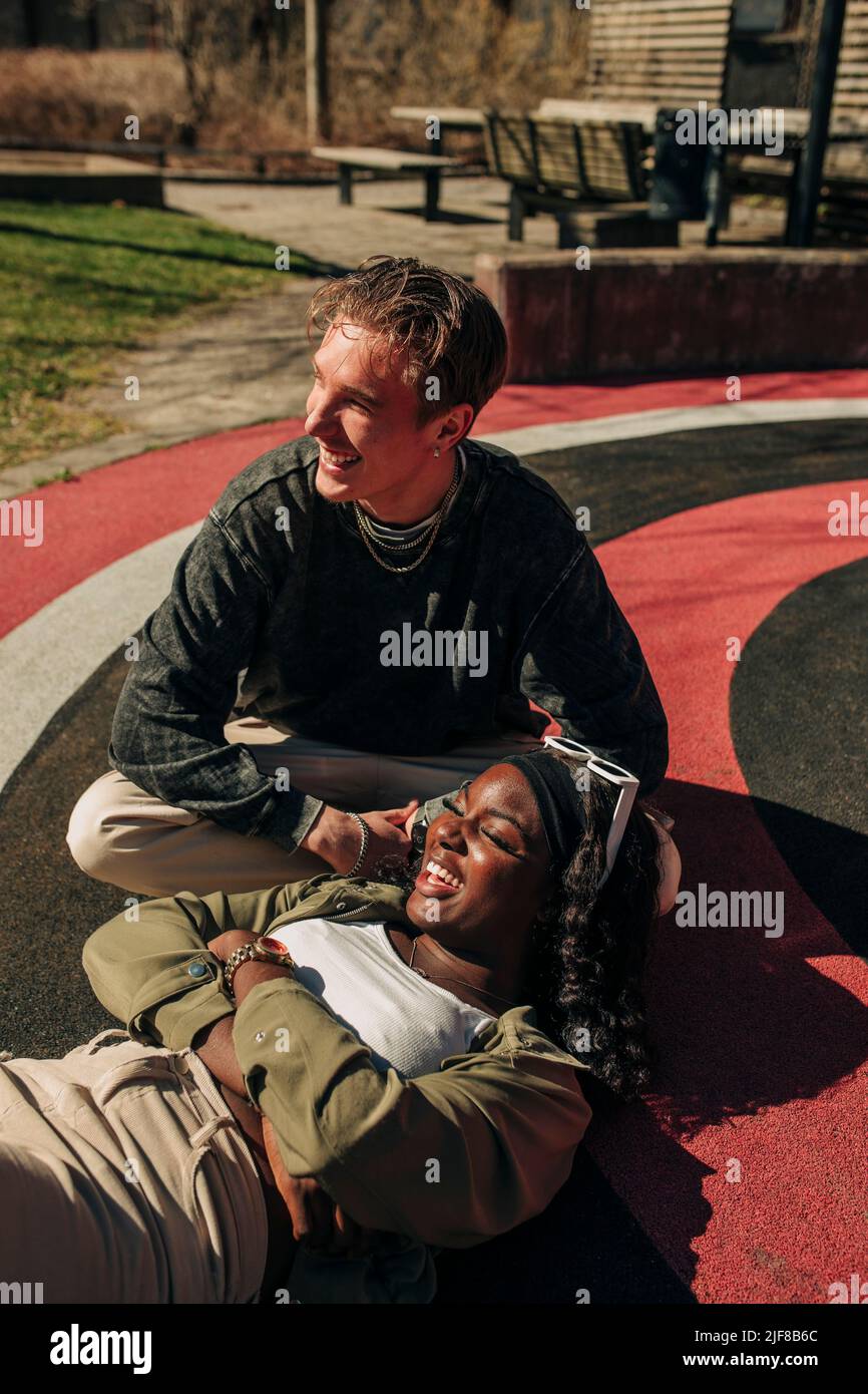 Smiling woman lying on lap of male friend relaxing in playground Stock Photo