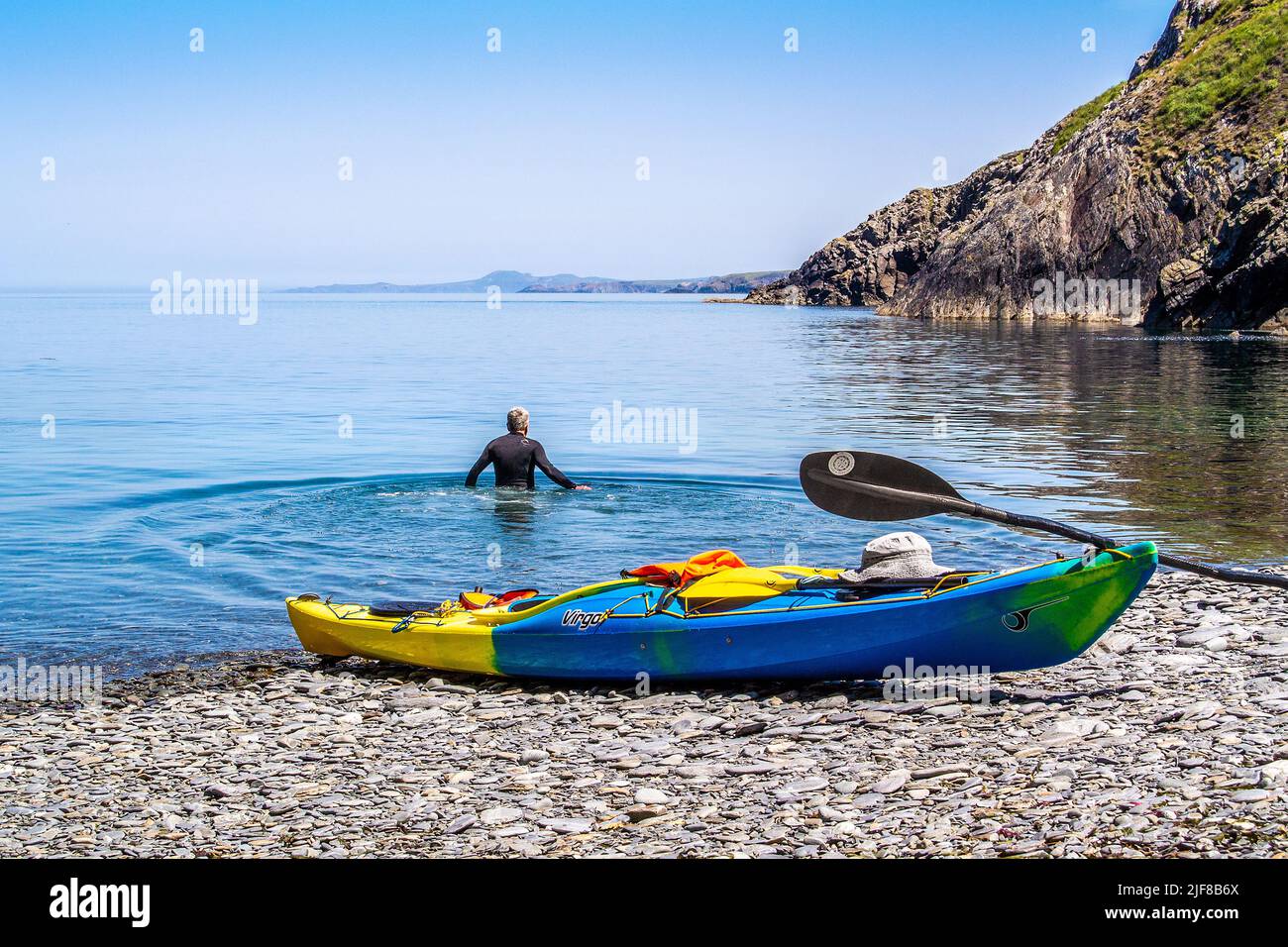 A kayaker swimming in the sea with kayak on beach, Pembrokeshire, Wales Stock Photo