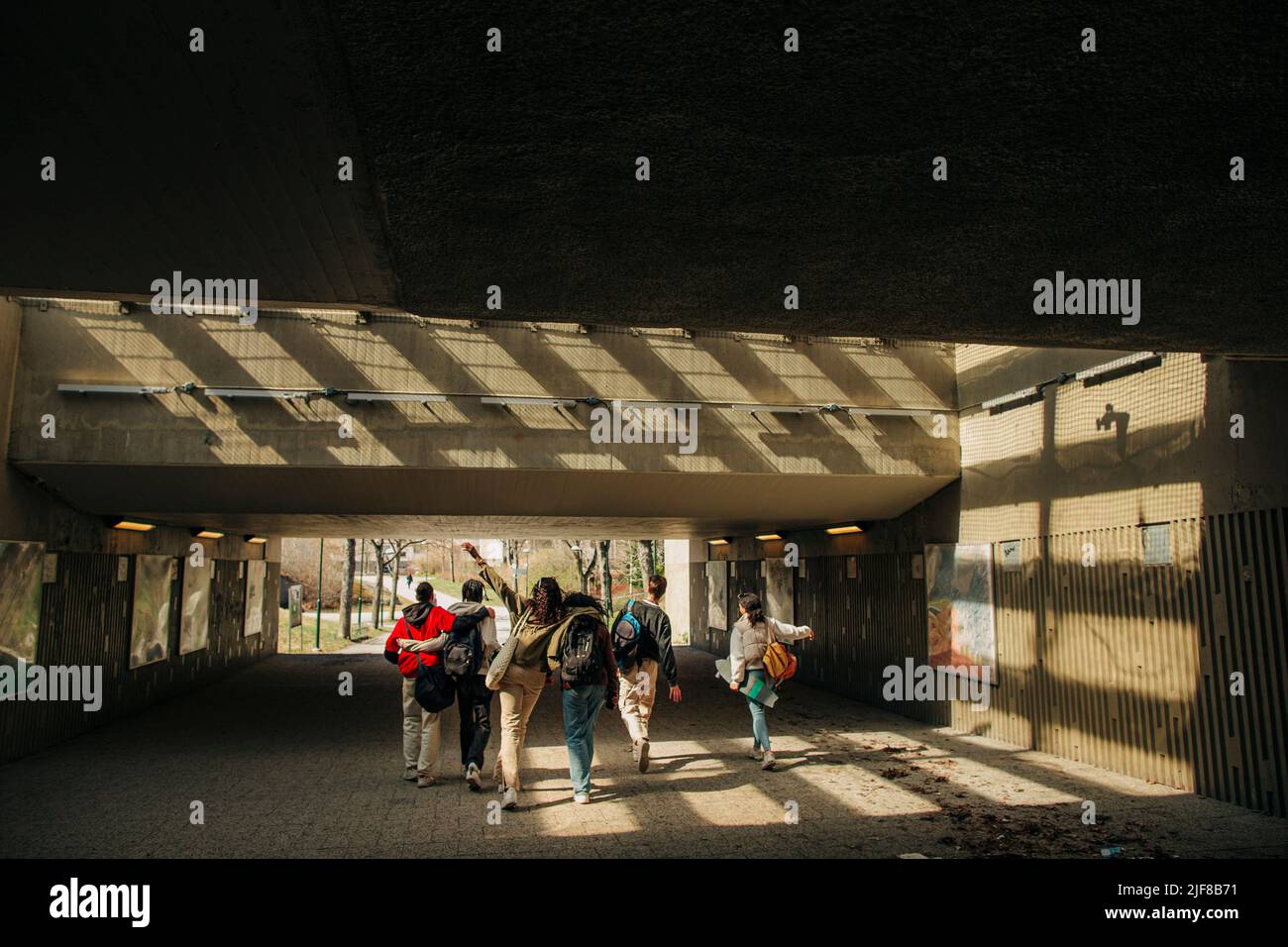 Rear view of multiracial friends walking together through underpass Stock Photo